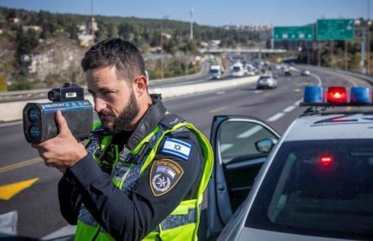 שוטר בשול הכביש אוכף מהירות מופרזת עם אקדח לייזר